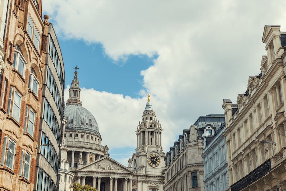 A detailed view of the classical architecture of St Paul's Cathedral in London, featuring its large domed roof with intricate carvings and columns, surrounded by modern brick and glass buildings on a